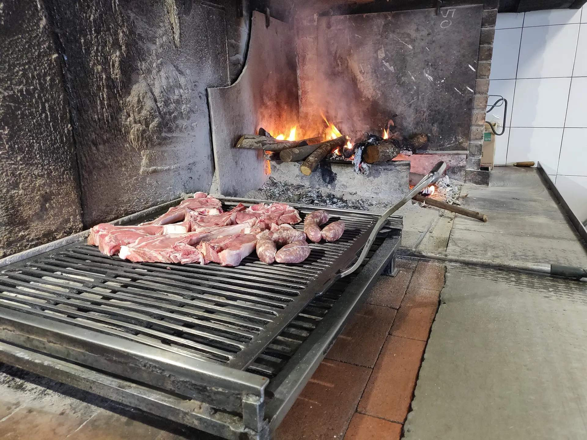 Carne e salsicce su griglia vicino a fuoco acceso.