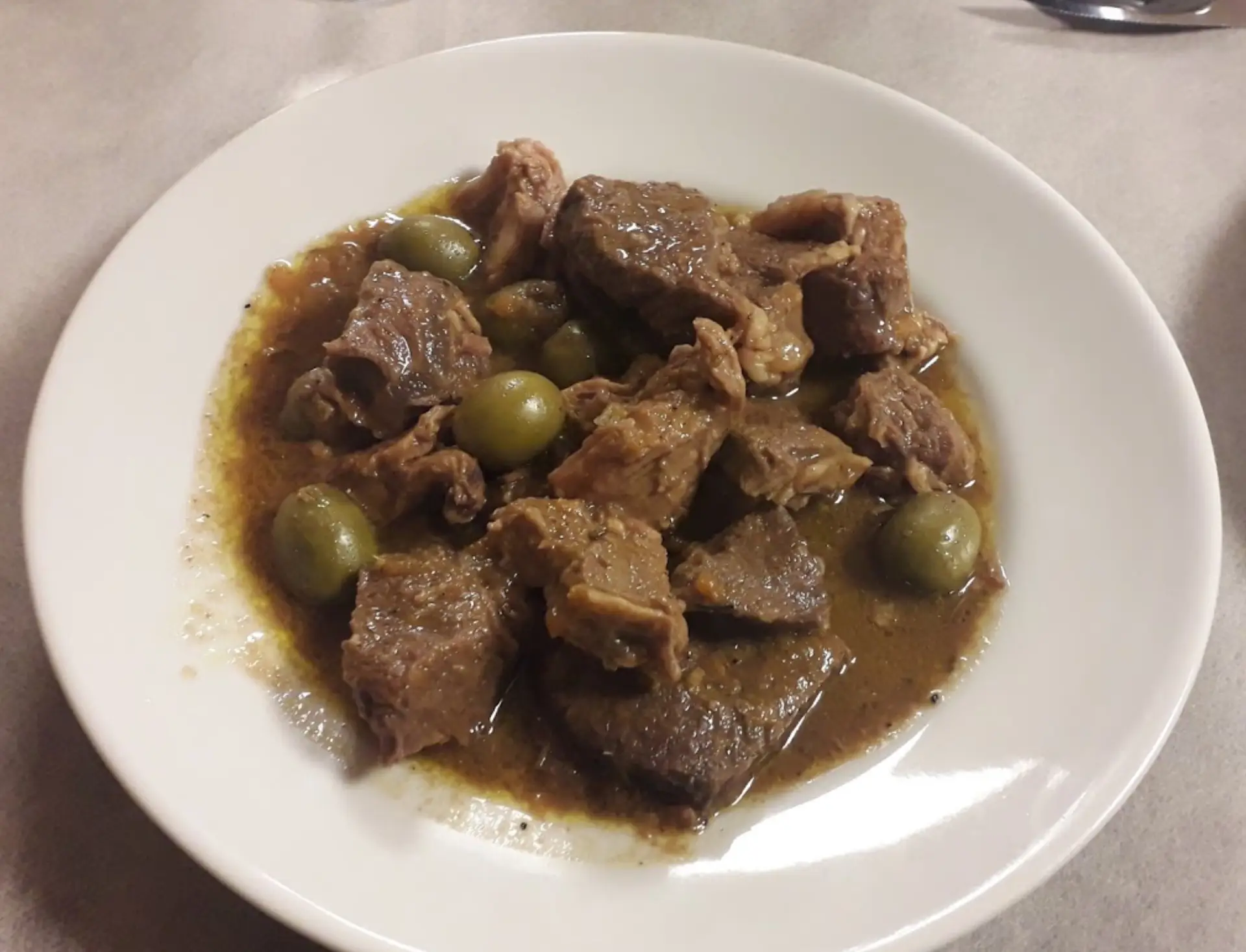 Spezzatino di carne con olive su piatto bianco.