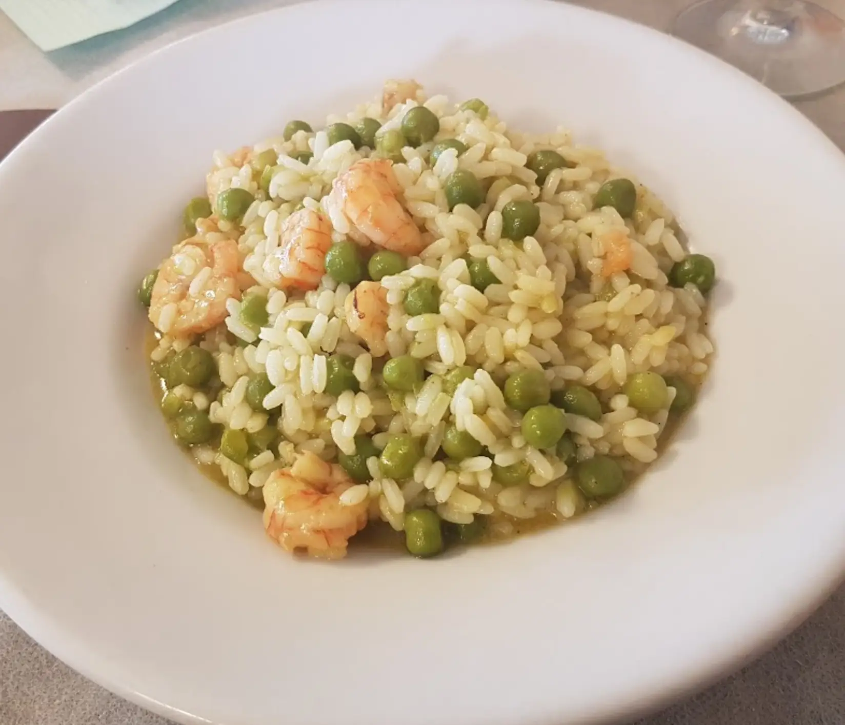 Risotto con gamberetti e piselli in un piatto bianco.