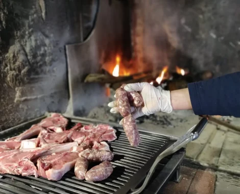 Carne e salsicce crude su griglia vicino al fuoco.